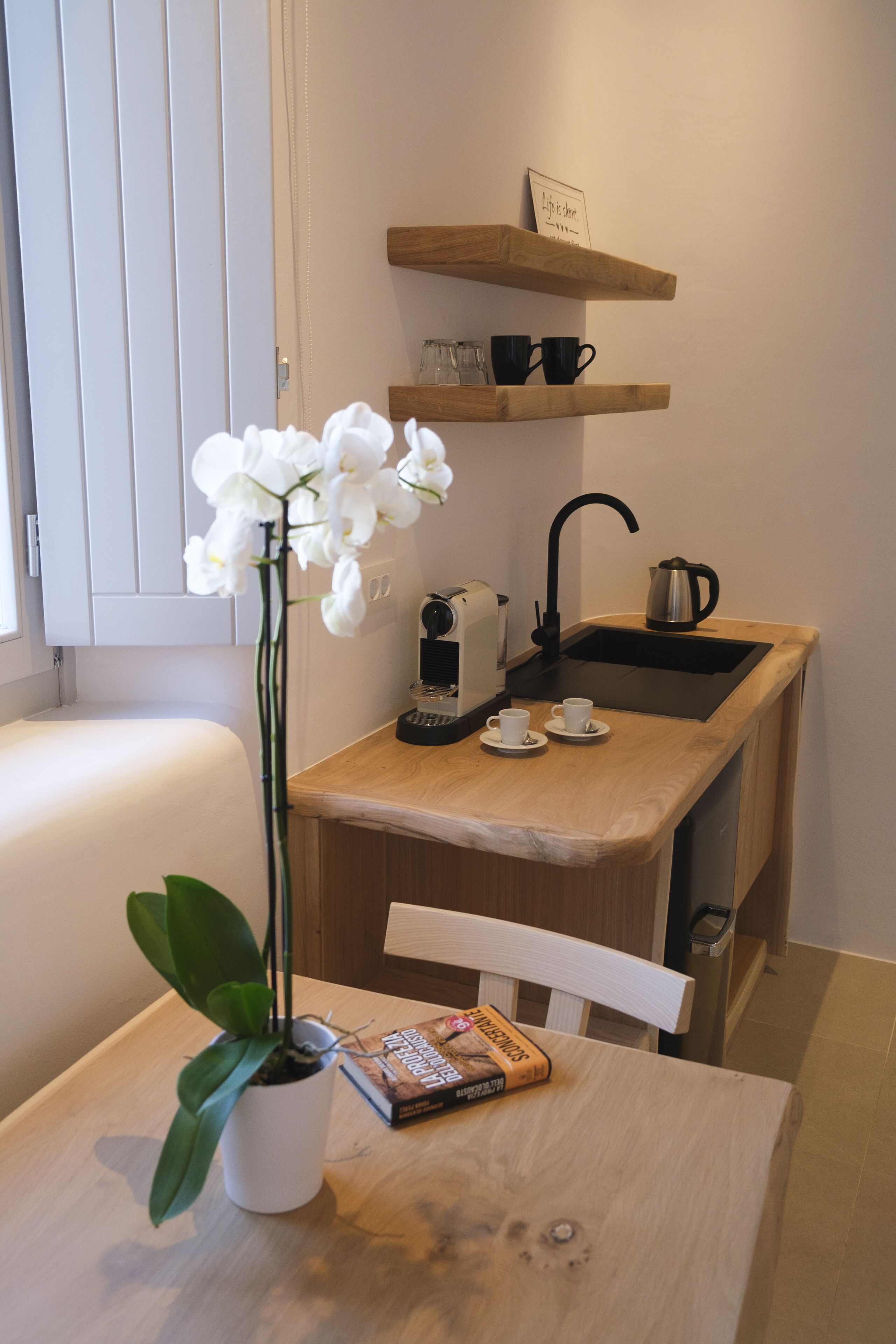 Een compacte kitchenette met een spoelbak, een koffiezetapparaat en een klein schap erboven.