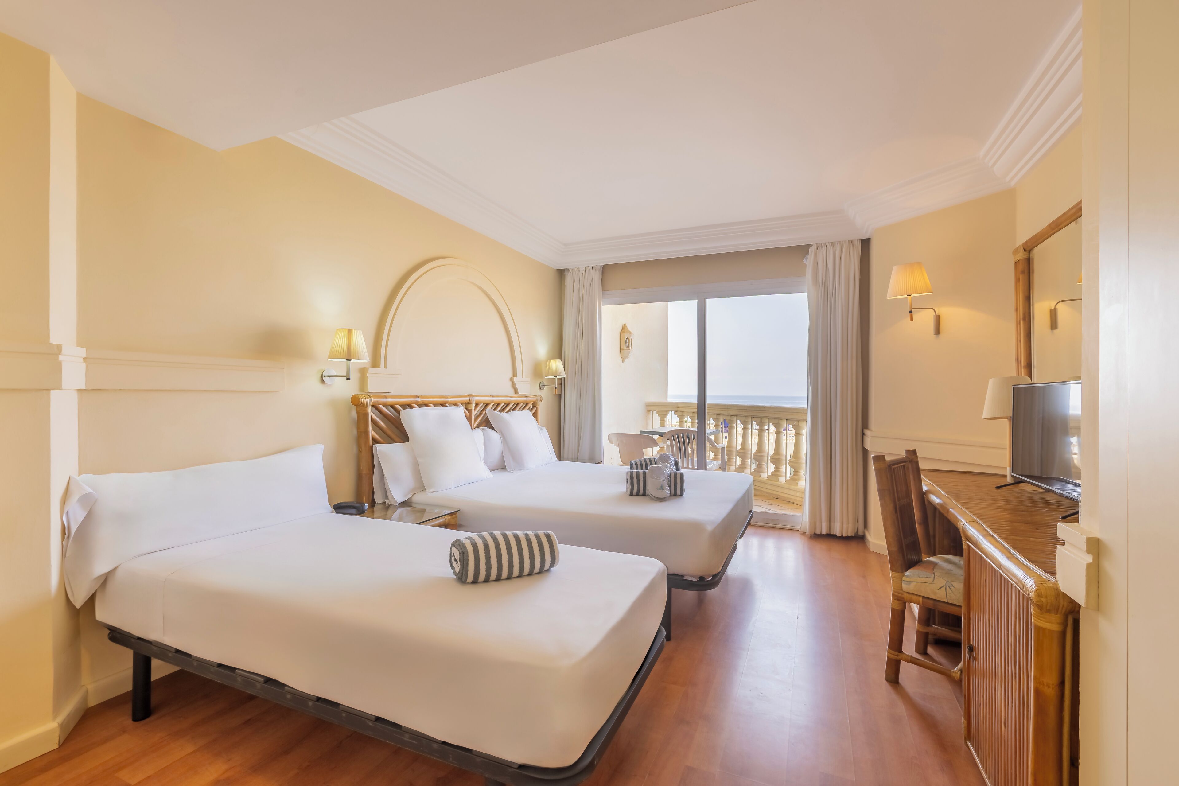 A hotel room with two beds, a balcony, a desk with a TV, and a chair.