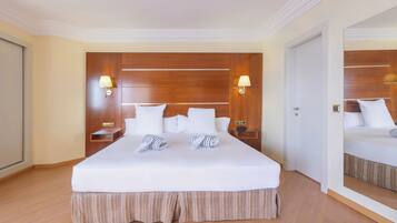 A hotel room with a large bed, wooden headboard, two bedside tables with lamps, and a mirror on the wall.