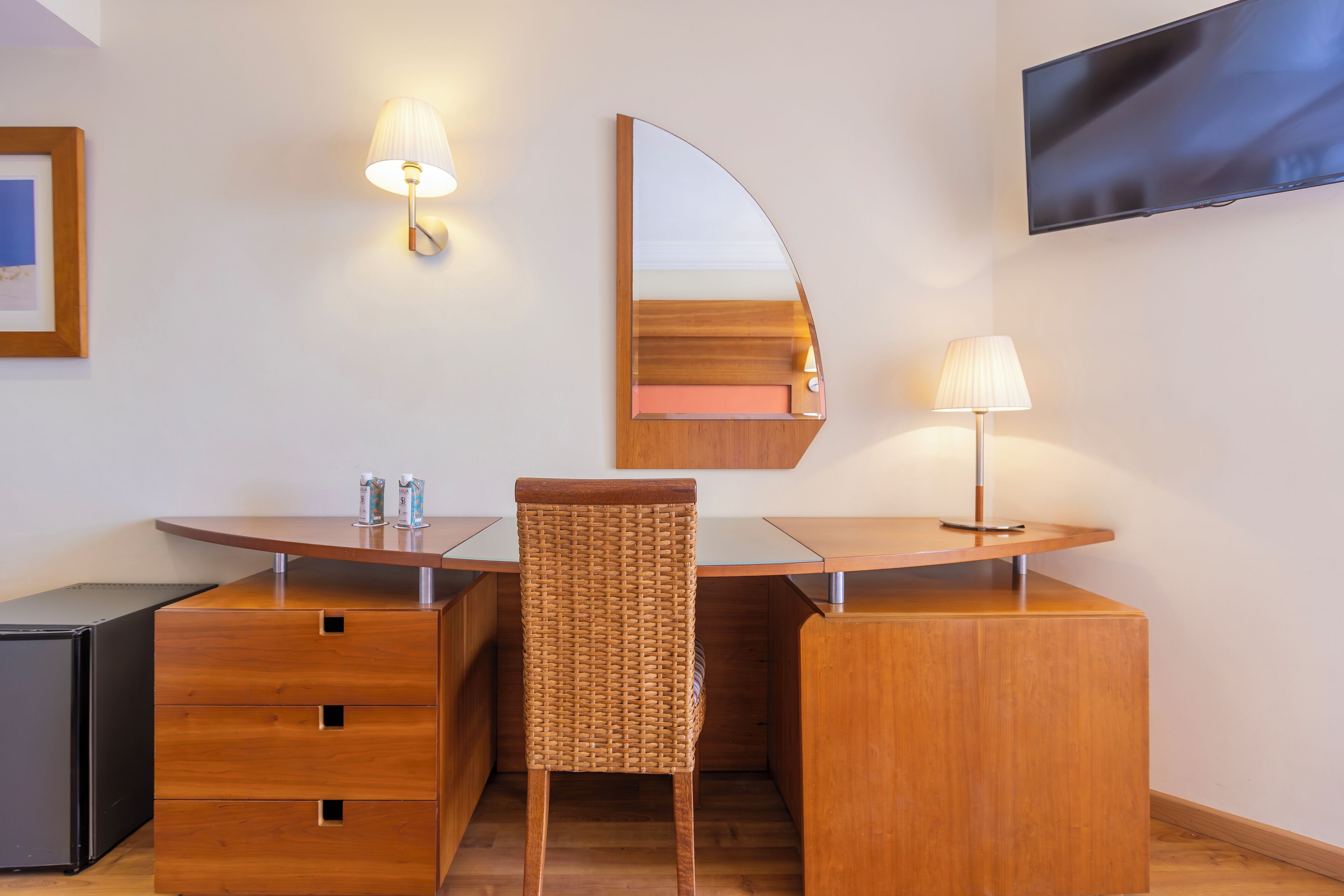 Una habitación de hotel moderna con un escritorio de madera, una silla, un televisor de pantalla plana y una lámpara fijada a la pared.