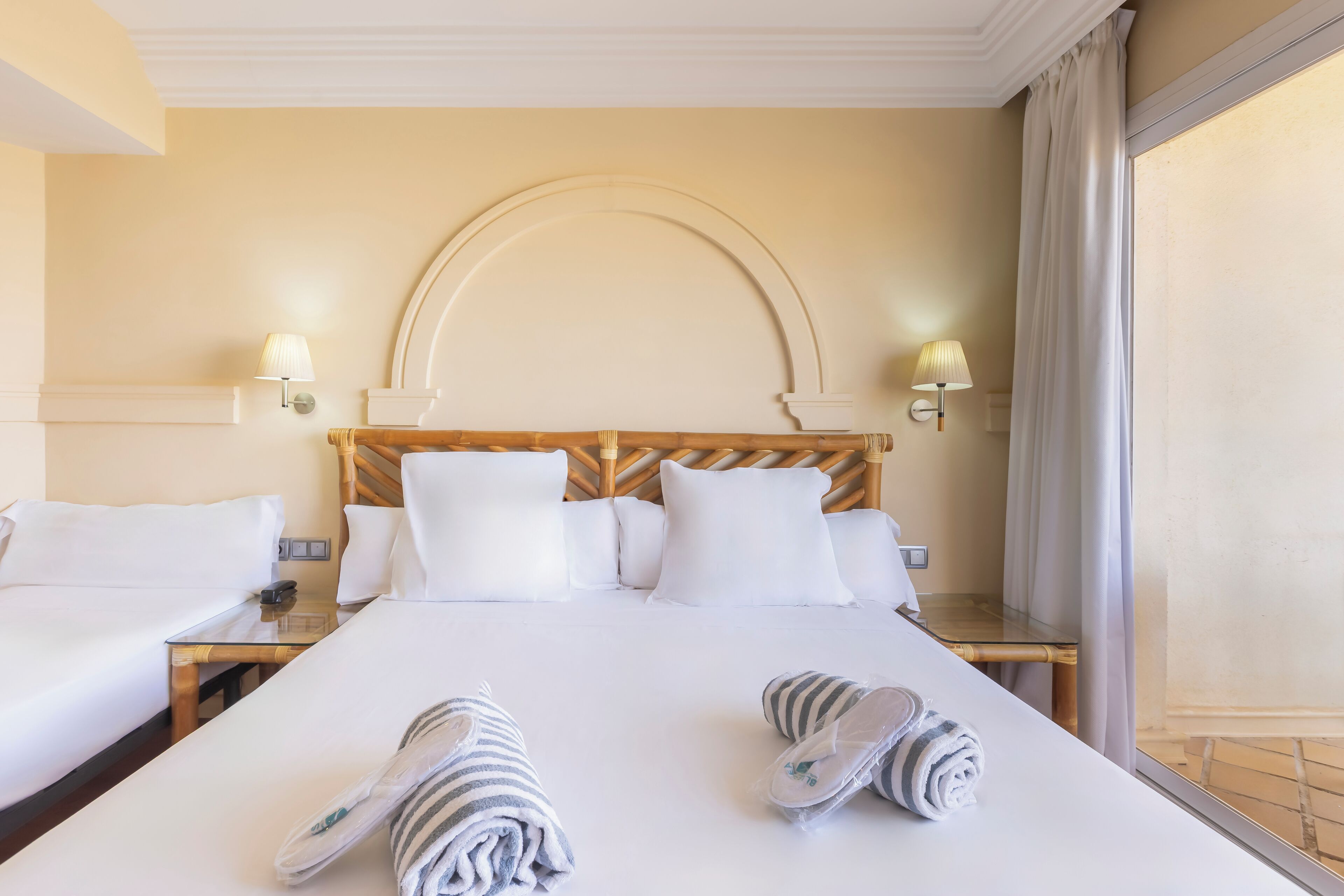 Habitación de hotel con una cama grande, dos mesitas de noche, cabecera de madera y dos lámparas fijadas a la pared.