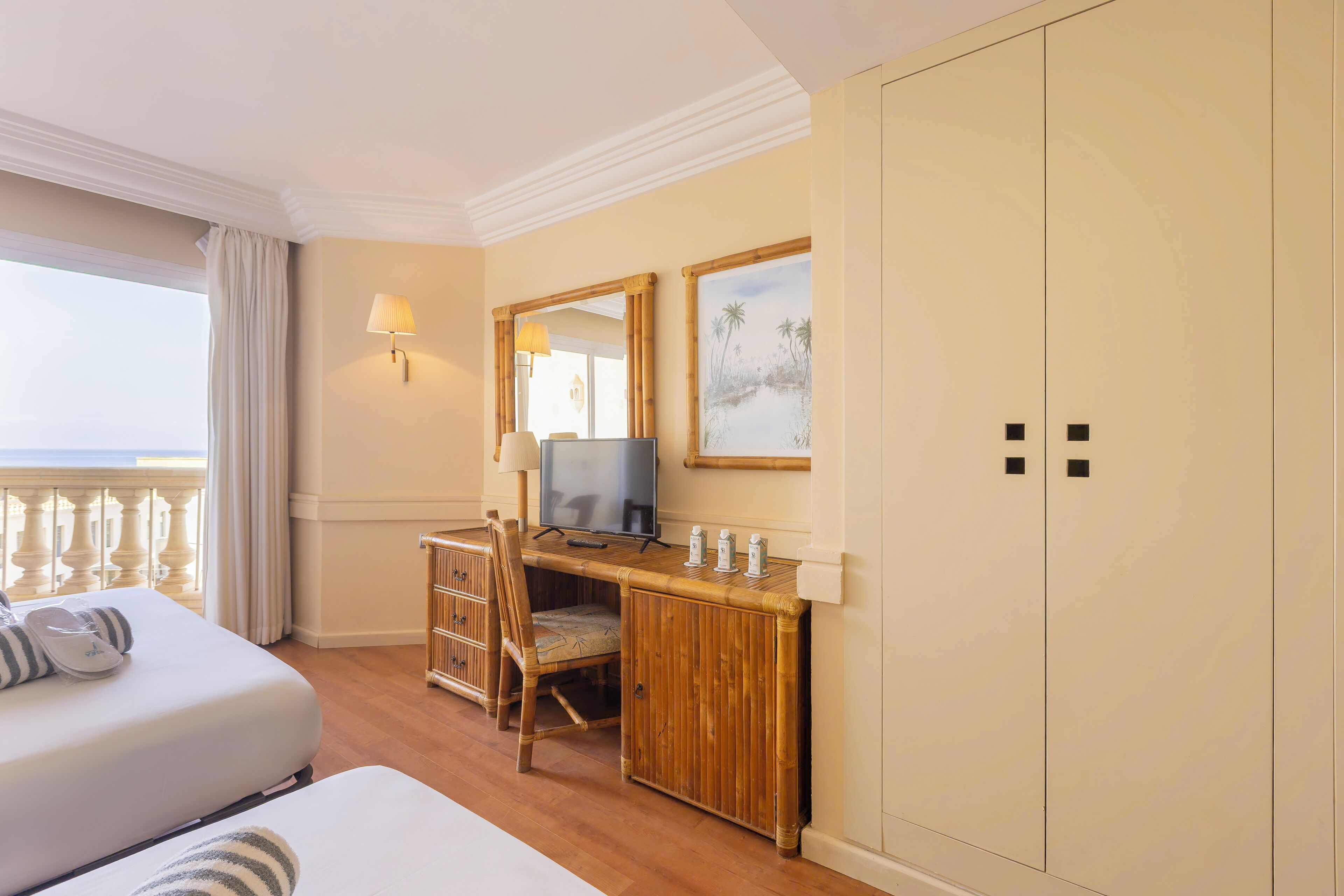 A hotel room with two beds, a desk with a chair, a television, a lamp, and a large wardrobe.
