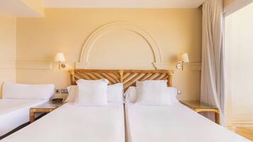 A hotel room with two single beds, a wooden headboard, bedside lamps, and a large window with curtains.