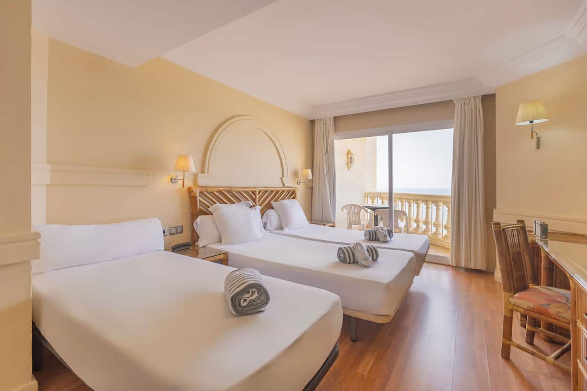 Habitación de hotel con dos camas, balcón y zona de comedor.