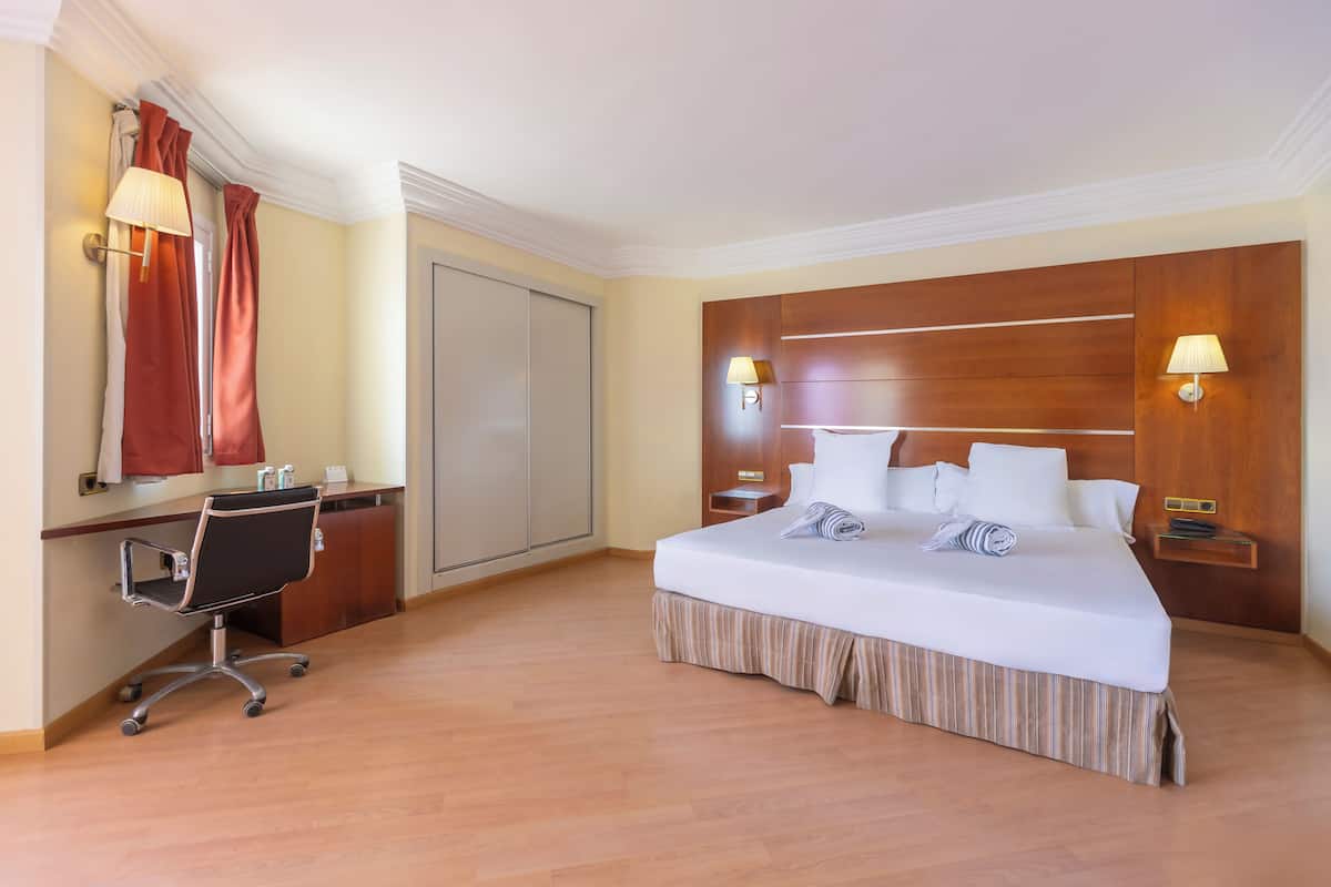 Una habitación de hotel con cama, escritorio, silla y dos lámparas de noche.