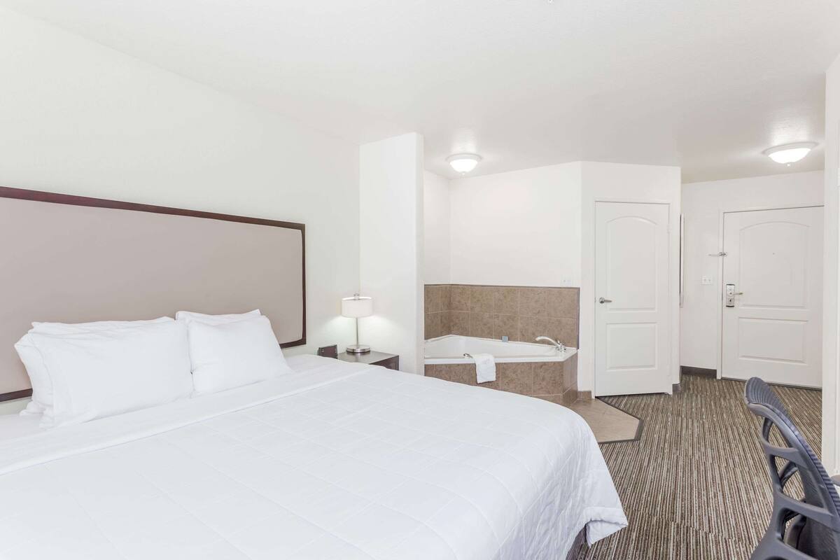 A hotel room with a bed, a desk, a lamp, a bathroom with a bathtub, and a door.