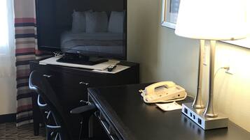 A hotel room with a bed, a desk with a computer, a telephone, and a lamp.