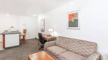 Een compacte hotelkamer met kitchenette, een sofa, een bureau met stoel en een bed.