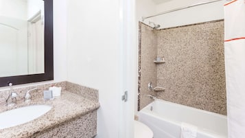 Un baño con lavamanos y encimera de granito, un espejo, ducha con pared de granito y una bañera blanca.