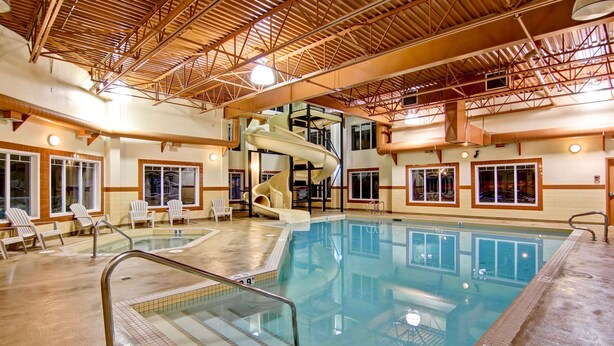 An indoor swimming pool with a slide, lounge chairs, and a high ceiling with visible beams. - Ramada by Wyndham Ponoka (Ponoka)