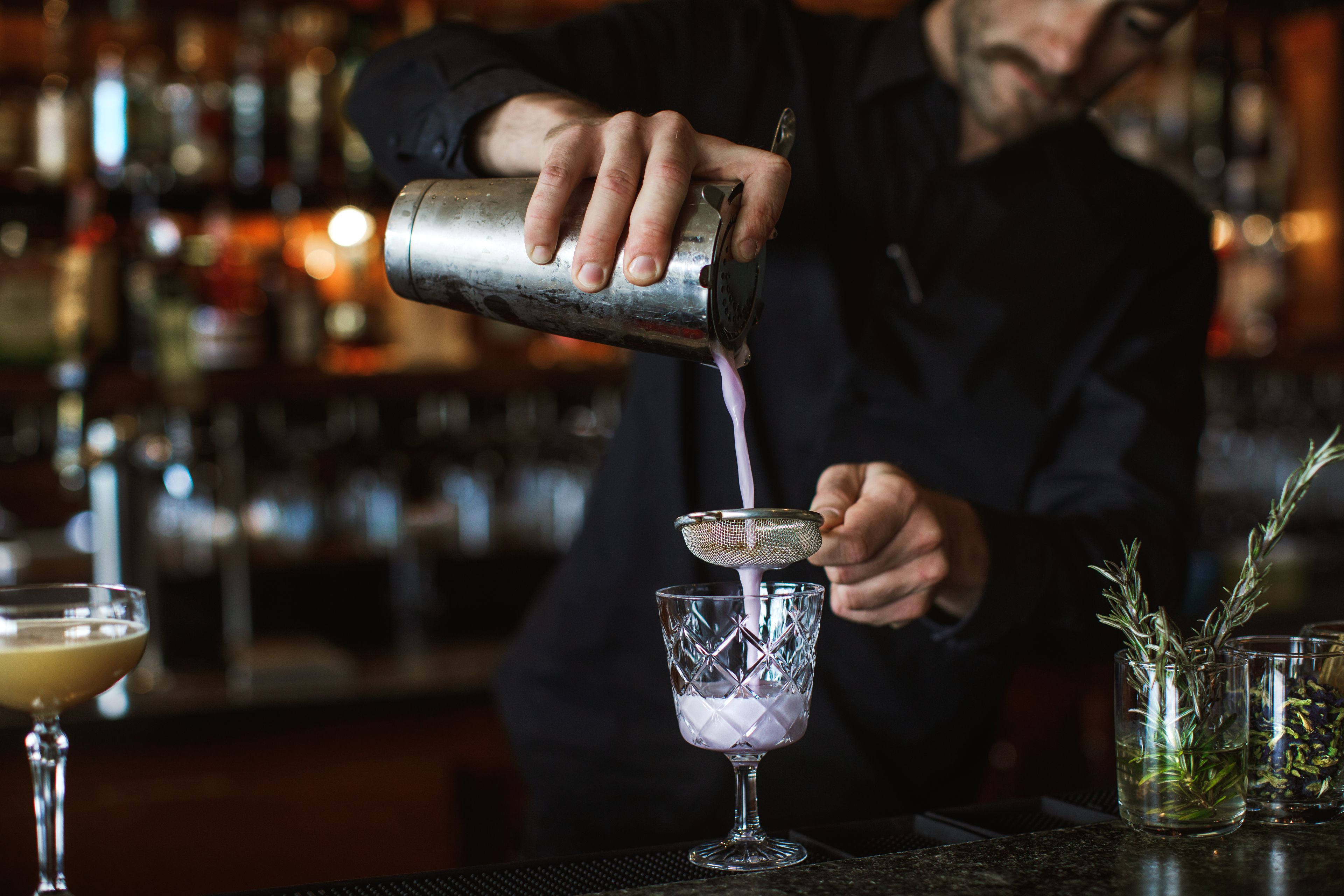 A bartender pouring a drink into a glass.