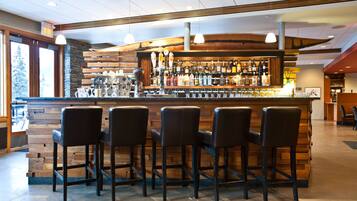A bar area with a wooden counter, multiple stools, and a variety of bottles and glasses.