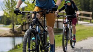 Two cyclists on a paved path with a lake and mountains in the background.