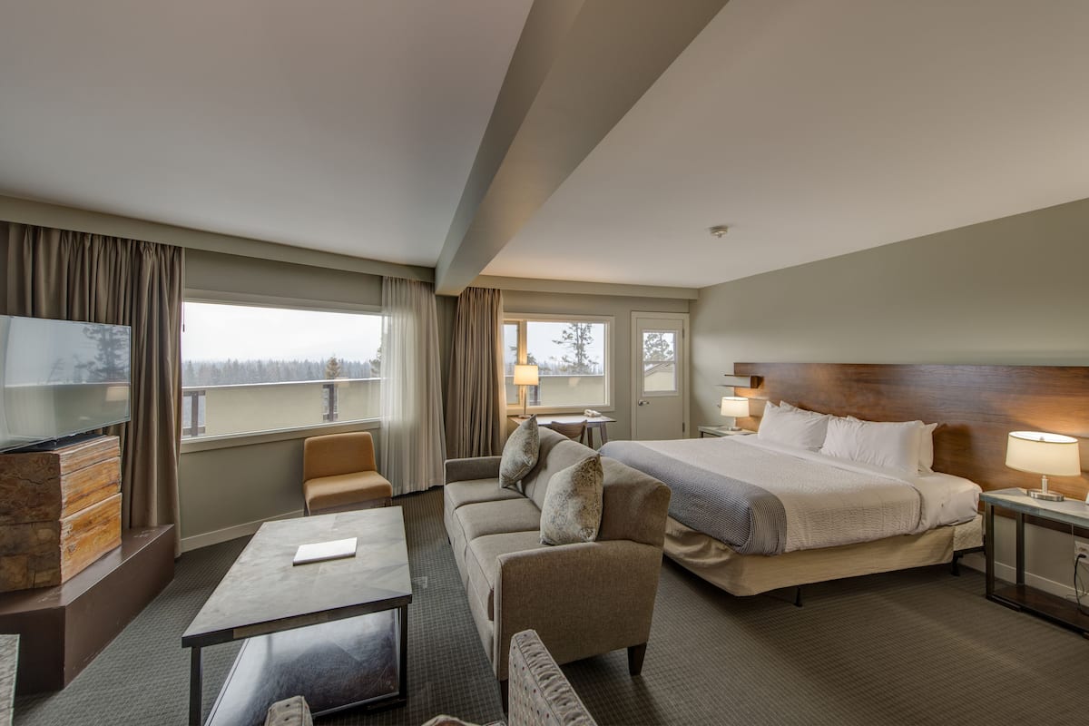 Une chambre d’hôtel avec un grand lit, un canapé, une télévision et un balcon avec des rideaux.