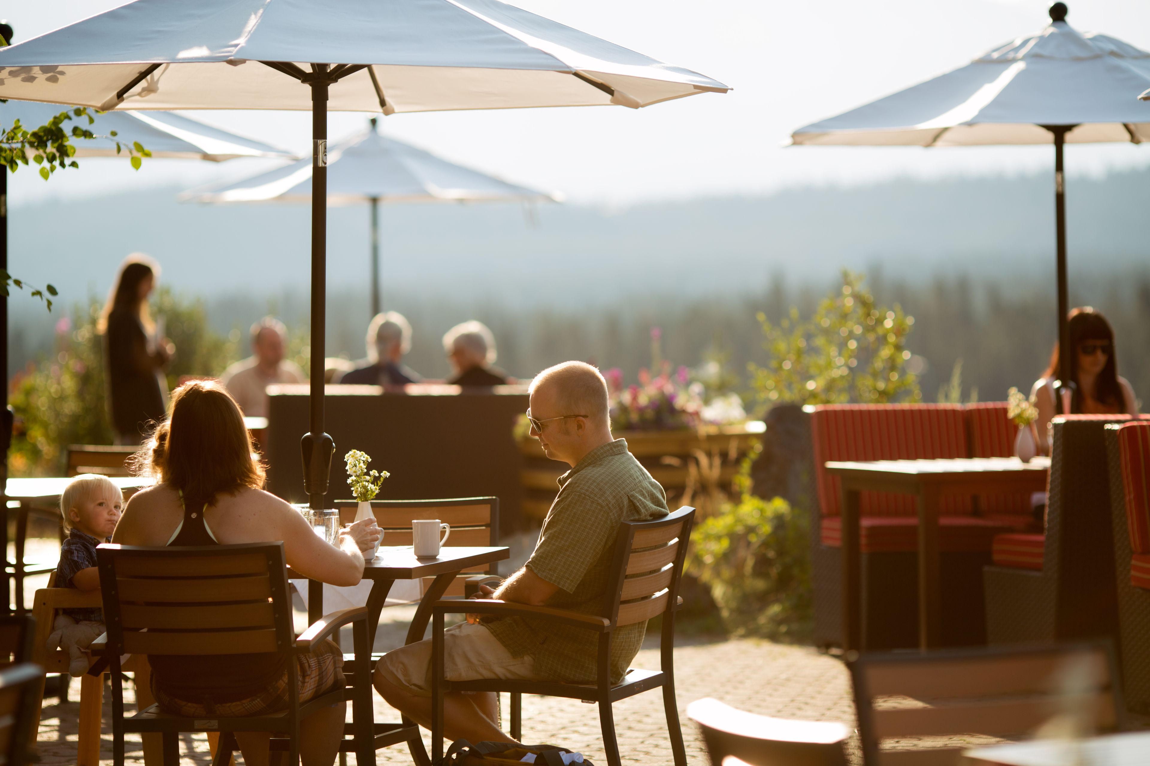 An outdoor dining area with tables and chairs, umbrellas, and a view of the mountains in the background.