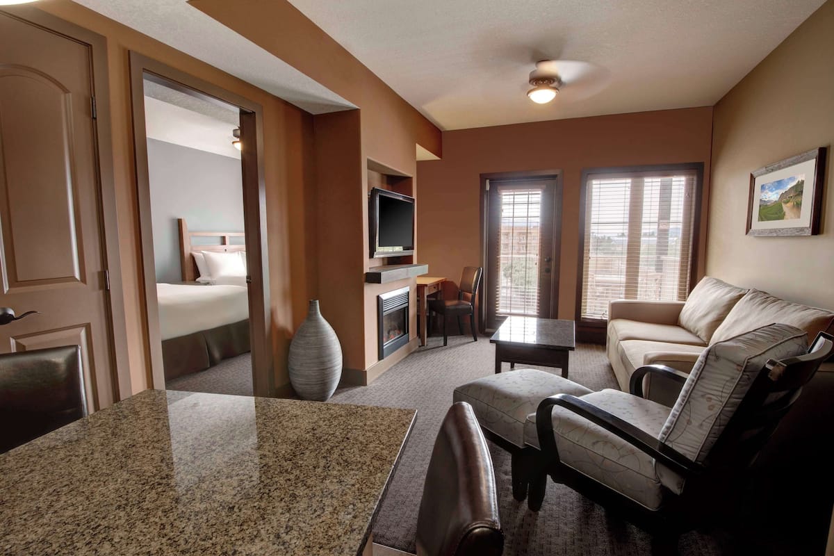 A hotel room with a bed, a TV, a fireplace, a dining table, and a sofa.