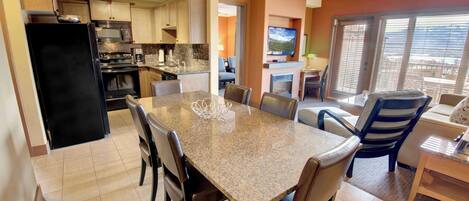 A modern kitchen with granite countertops, a black refrigerator, and a dining area with a granite table and leather chairs.