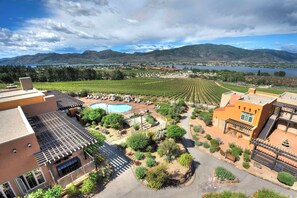 A hotel with a pool, outdoor seating, and a view of vineyards and mountains.