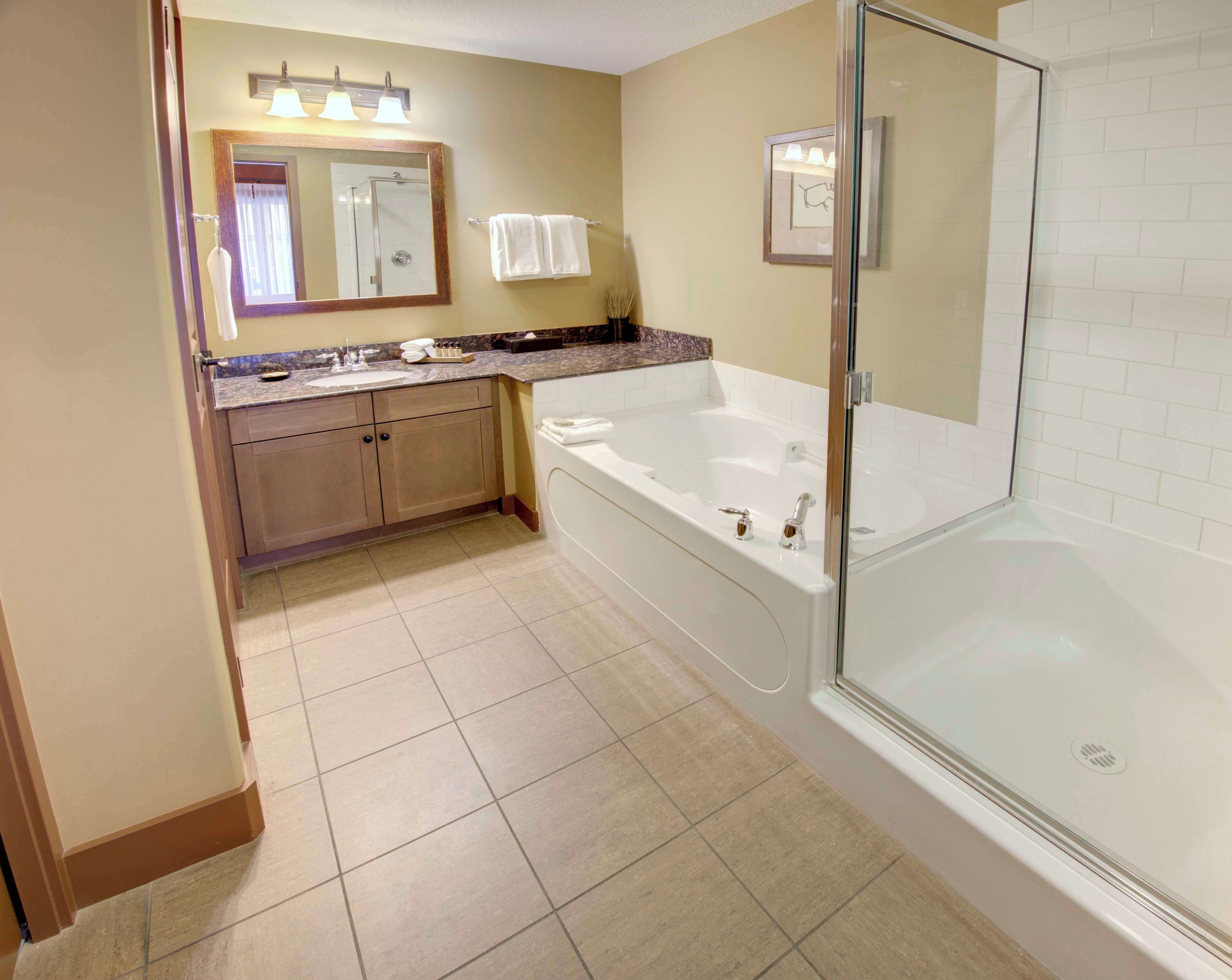Une salle de bain moderne dotée d’une grande baignoire, d’une zone de douche et d’un meuble-lavabo avec un miroir et un porte-serviettes.