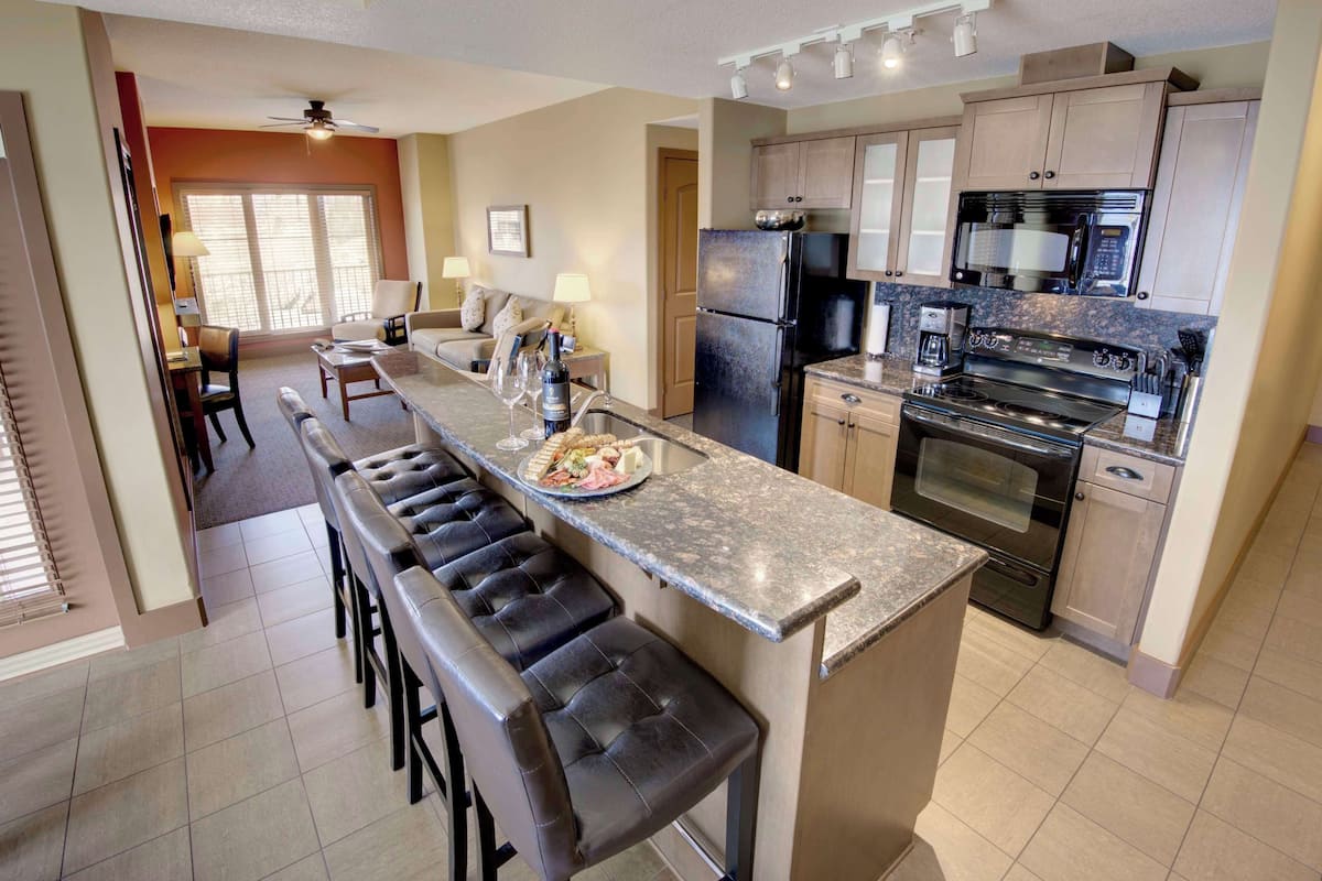 A modern kitchen with a central island, bar stools, a refrigerator, stove, microwave, and a dining area with a sofa and table.