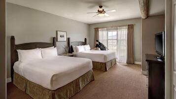 A hotel room with two beds, a ceiling fan, a TV, and a window with curtains.
