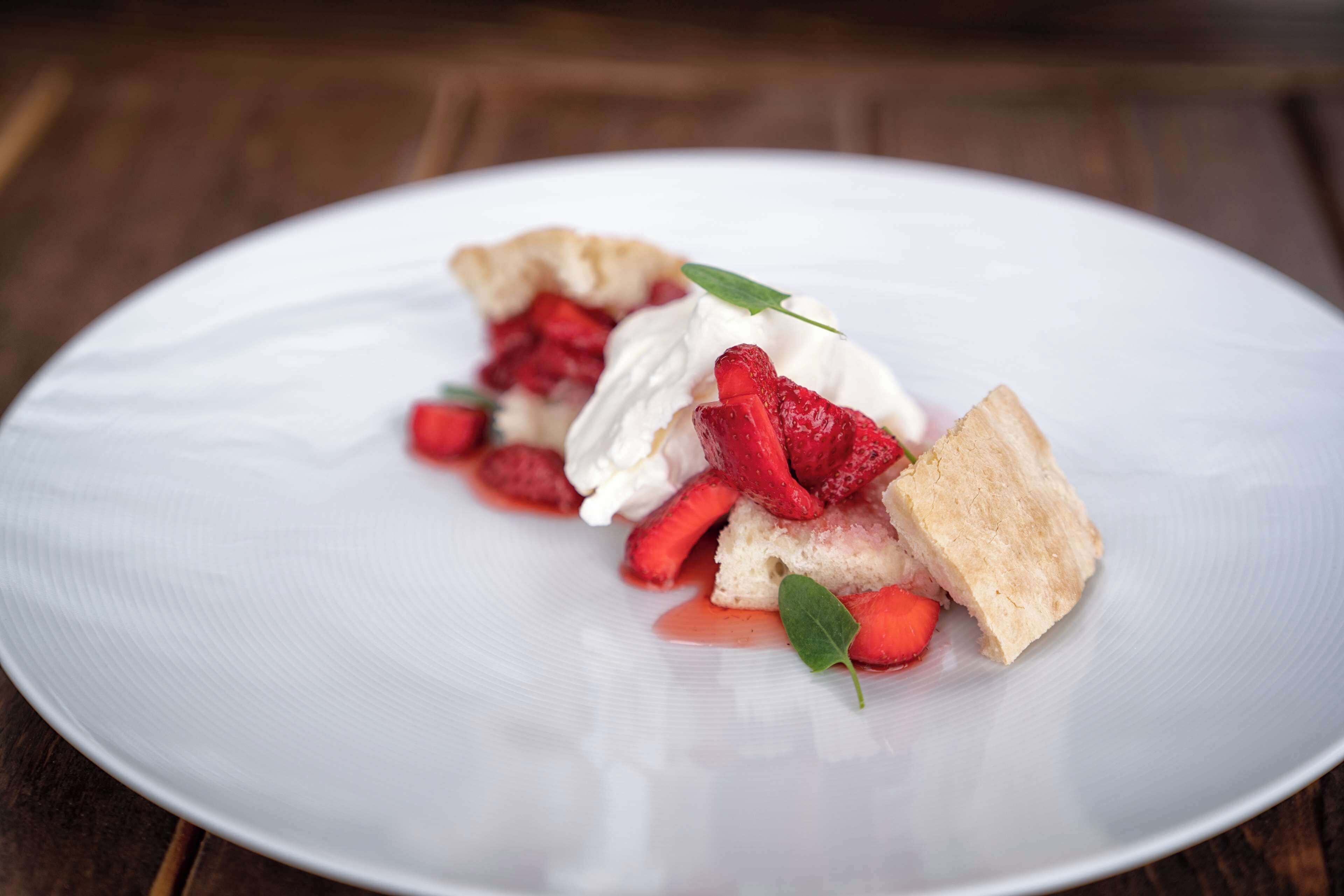 A dessert on a white plate with strawberries and whipped cream.