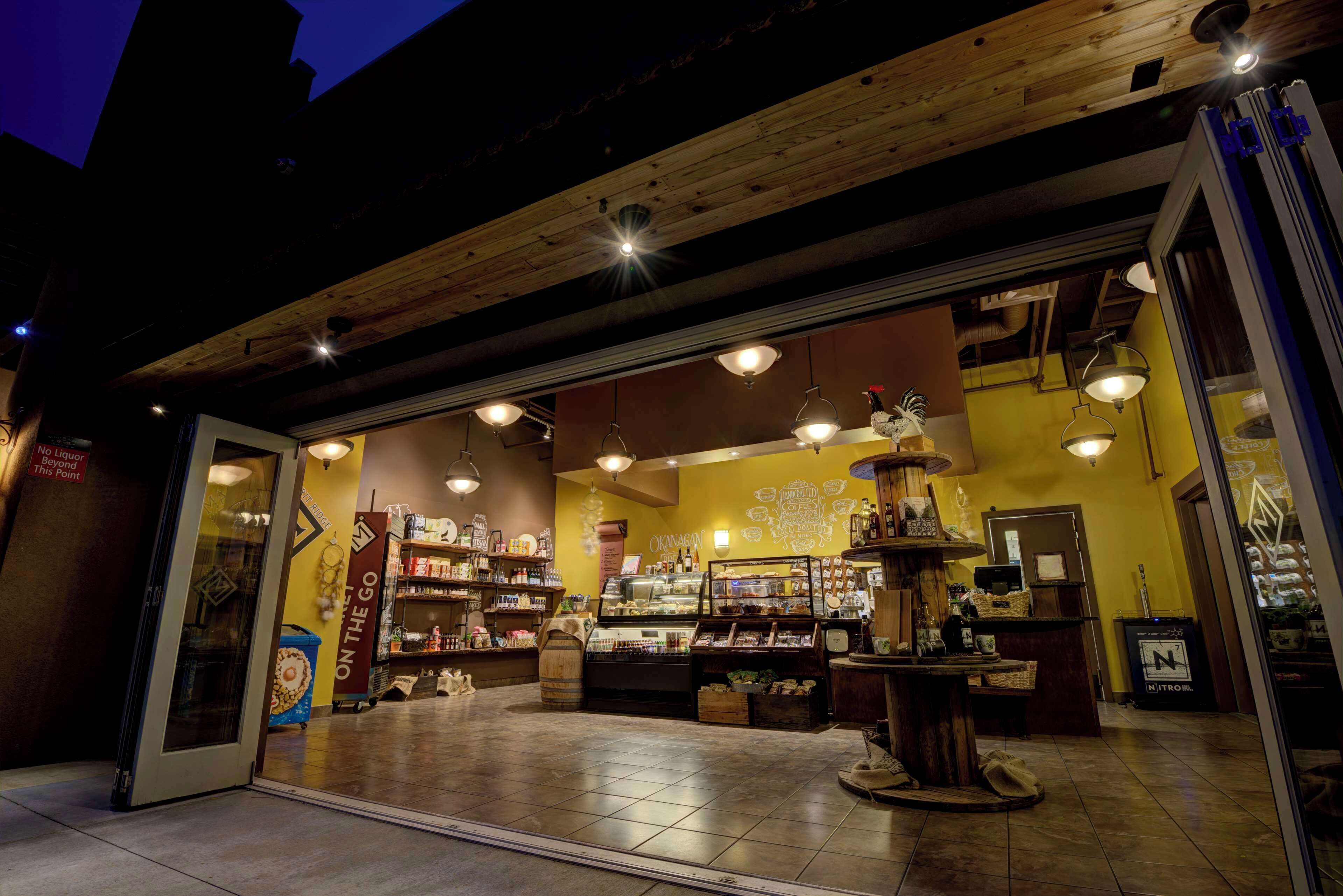 A cozy café with a wooden ceiling and warm lighting, featuring a display counter and shelves stocked with various items.