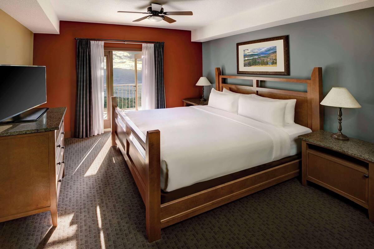 A hotel room with a large bed, a television, a desk, and a balcony with curtains.