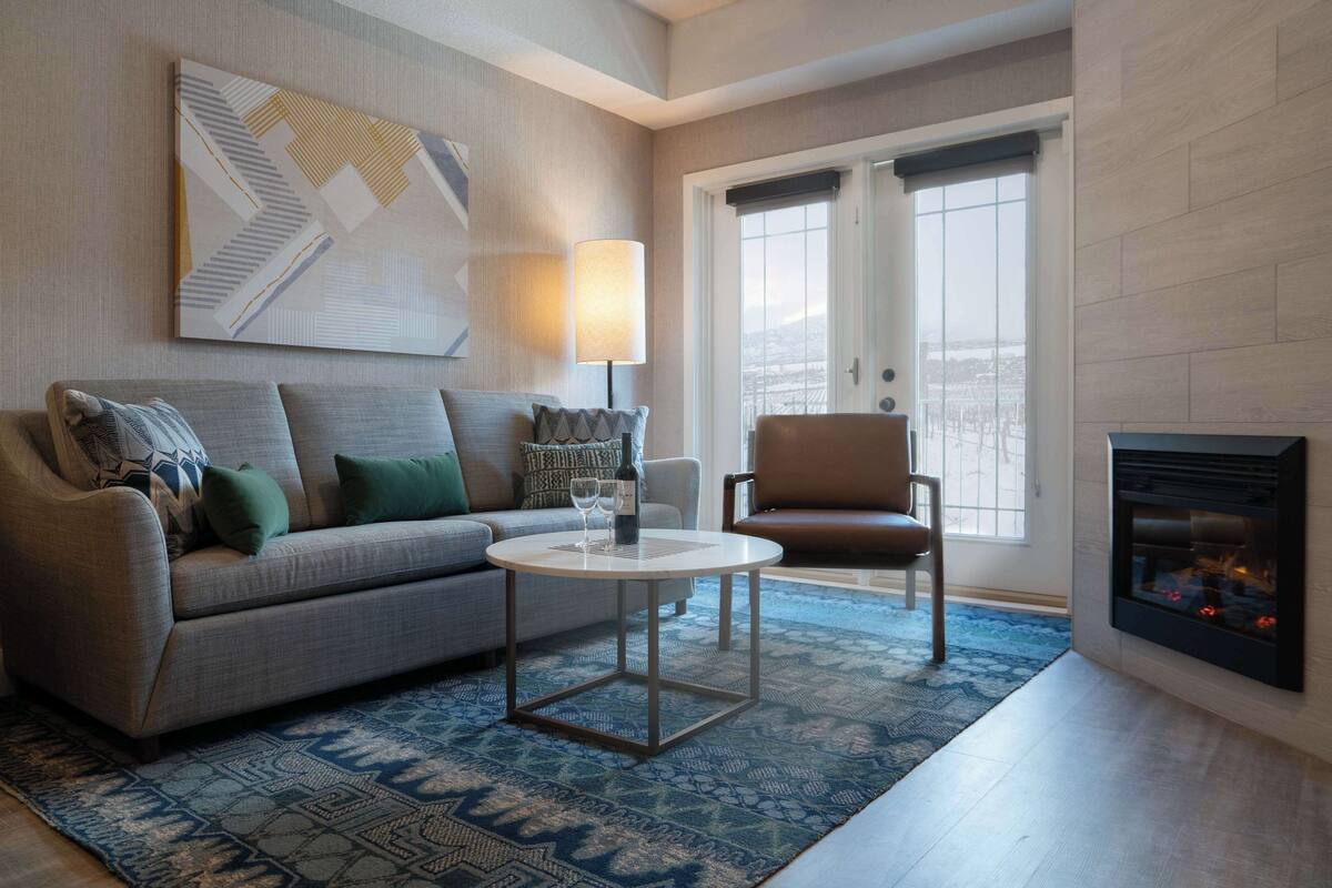 A living room with a sofa, armchair, coffee table, fireplace, and a large window.