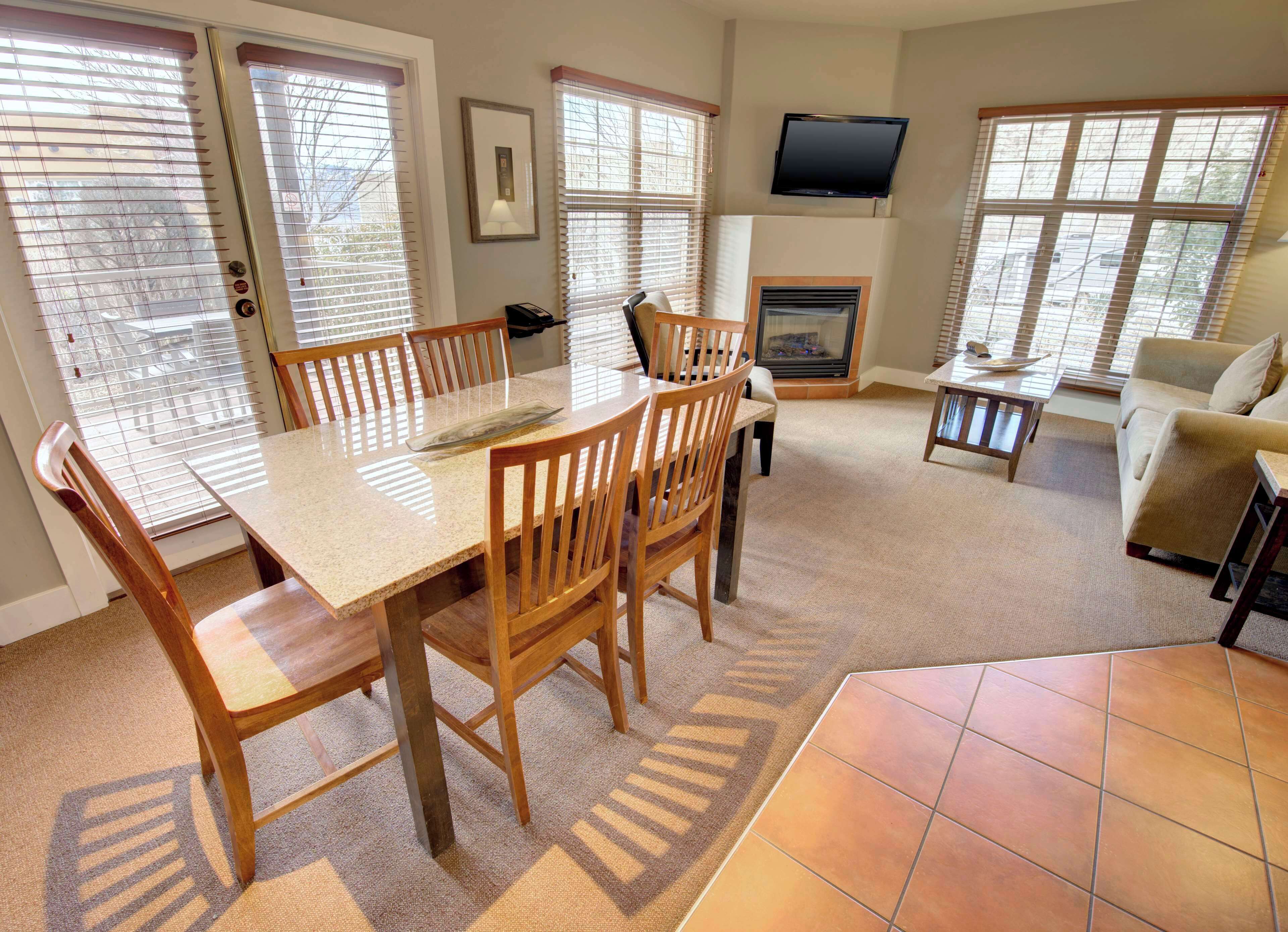 A spacious living room with a fireplace, a television mounted above it, and a dining area with wooden chairs and a glass-top table.