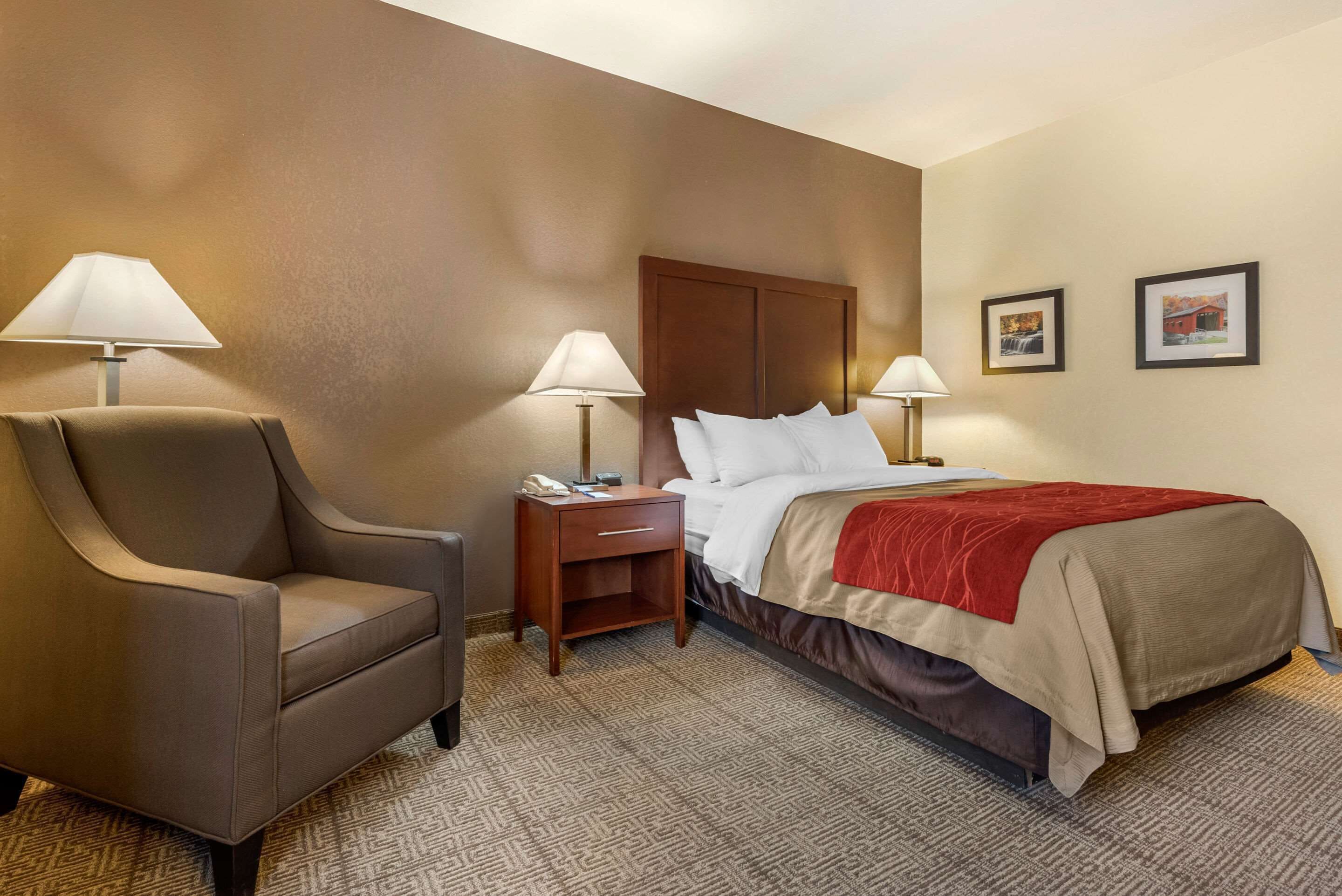 Ein Hotelzimmer mit einem Bett, zwei Nachttischlampen, einem Sessel, einem Nachttisch und zwei gerahmten Bildern an der Wand.