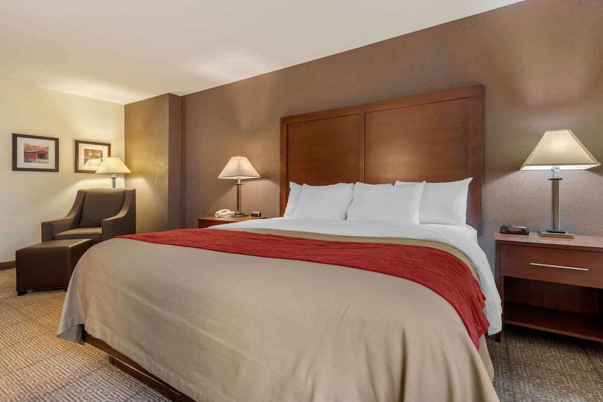 A hotel room with a large bed, a chair, two bedside tables with lamps, and framed pictures on the wall.