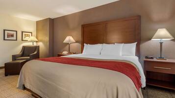 A hotel room with a large bed, a chair, two bedside tables with lamps, and framed pictures on the wall.