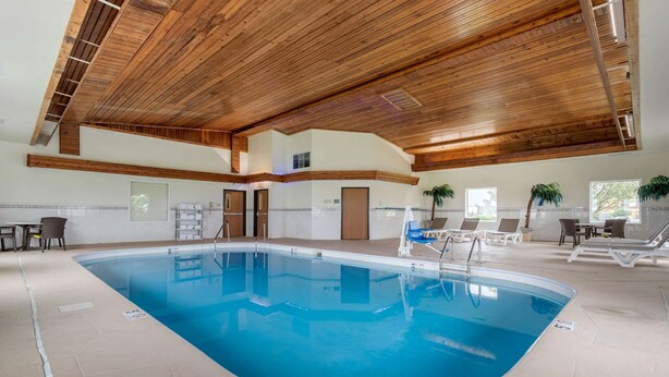 An indoor swimming pool with wooden ceiling beams, a tiled floor, and lounge chairs around the pool.