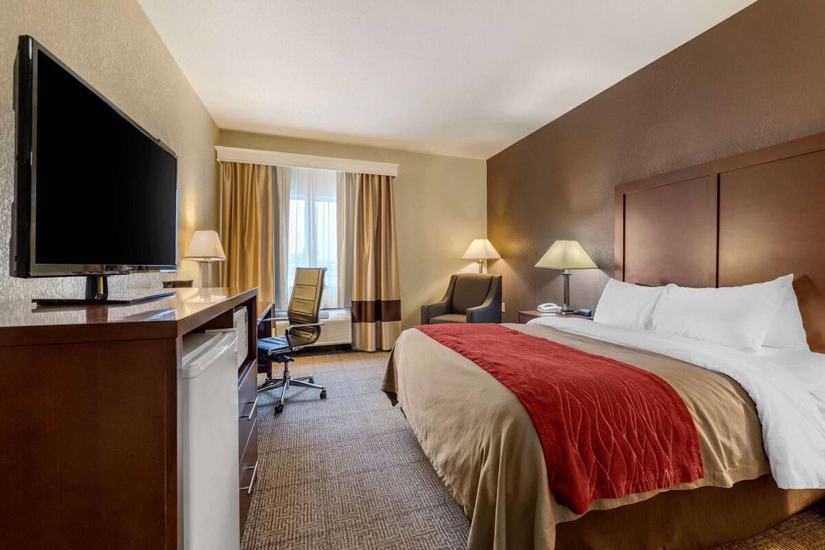 A hotel room with a bed, desk, TV, and two chairs.