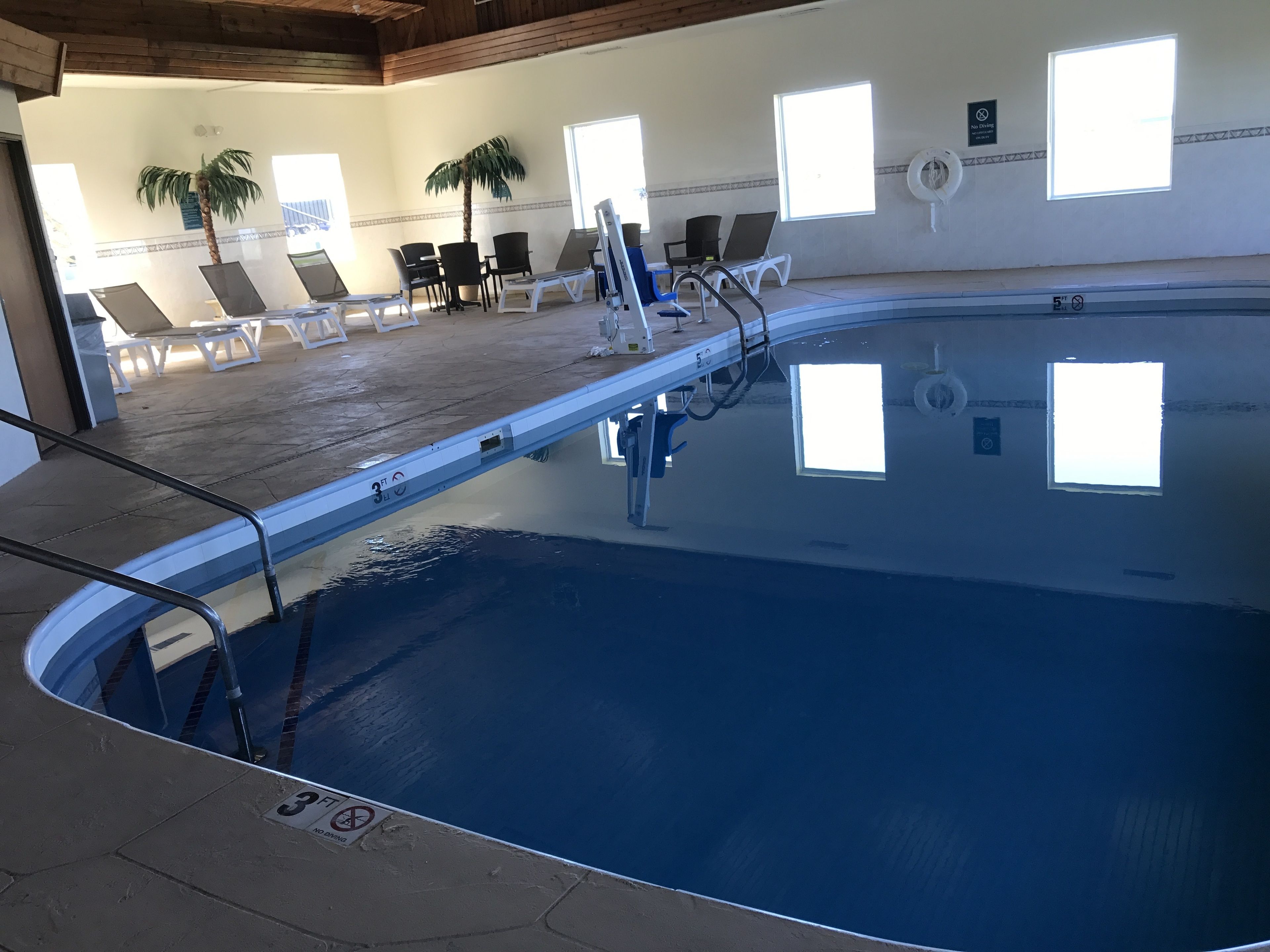 An indoor swimming pool with clear water, a diving board, and lounge chairs.