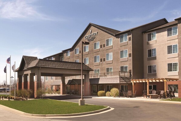 A multi-story hotel with a covered entrance, outdoor seating area, and a clear sky.
