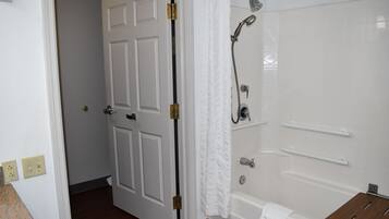 Un bagno con una vasca da bagno bianca, una doccia e uno scaffale in legno.