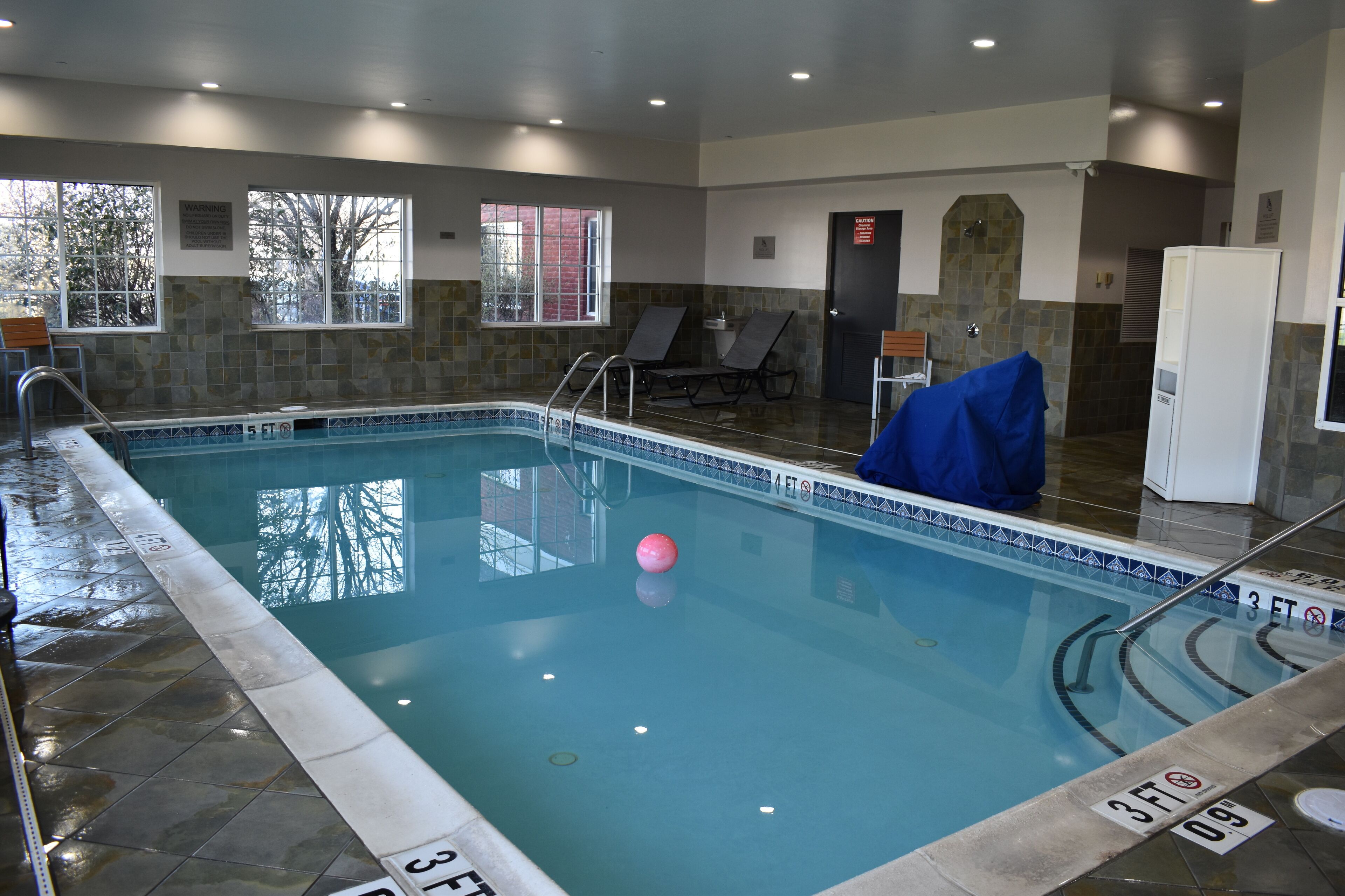 An indoor swimming pool with clear water, marked depth lines, and a pink ball.