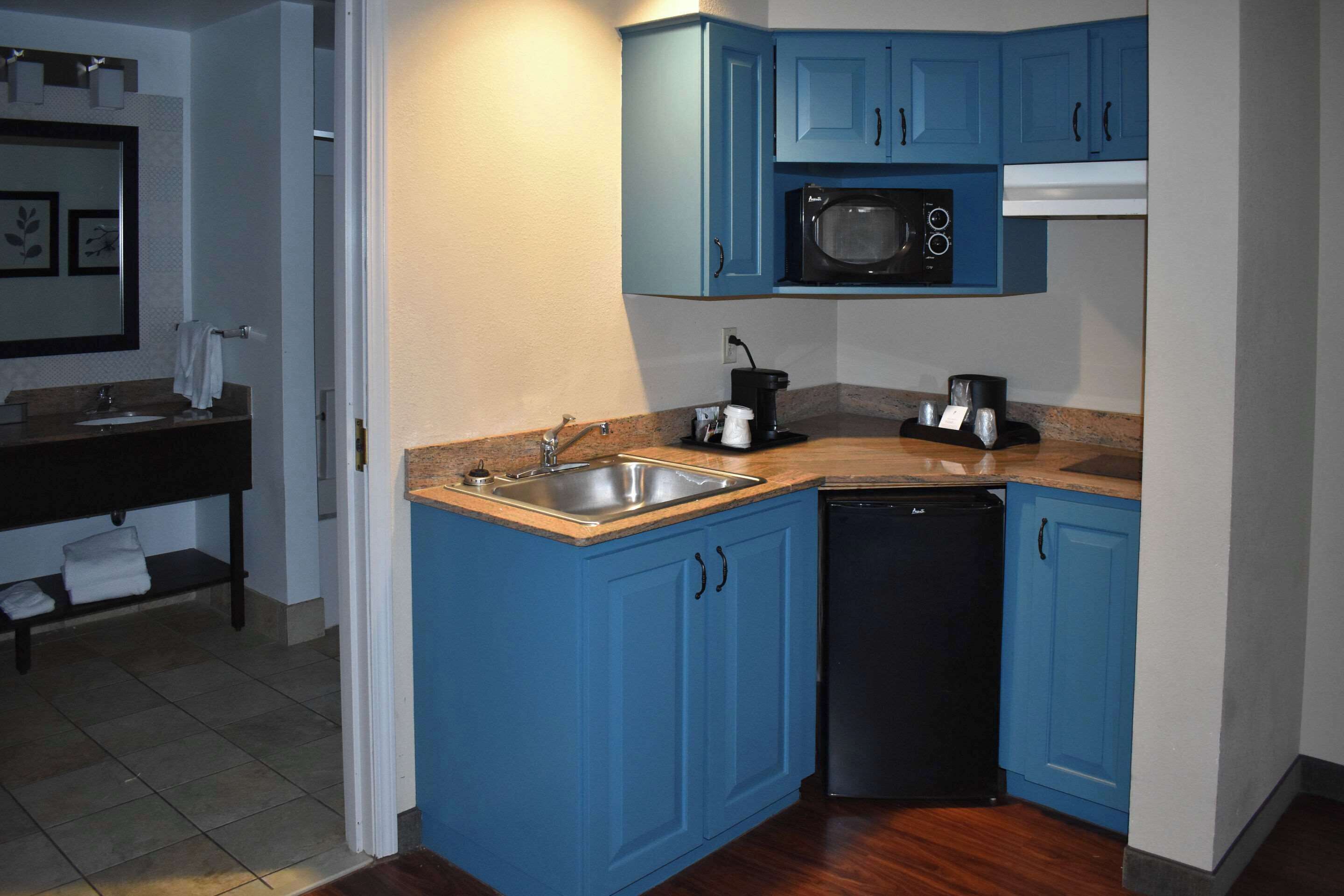 A compact kitchen with blue cabinets, a microwave, a coffee maker, and a dishwasher.