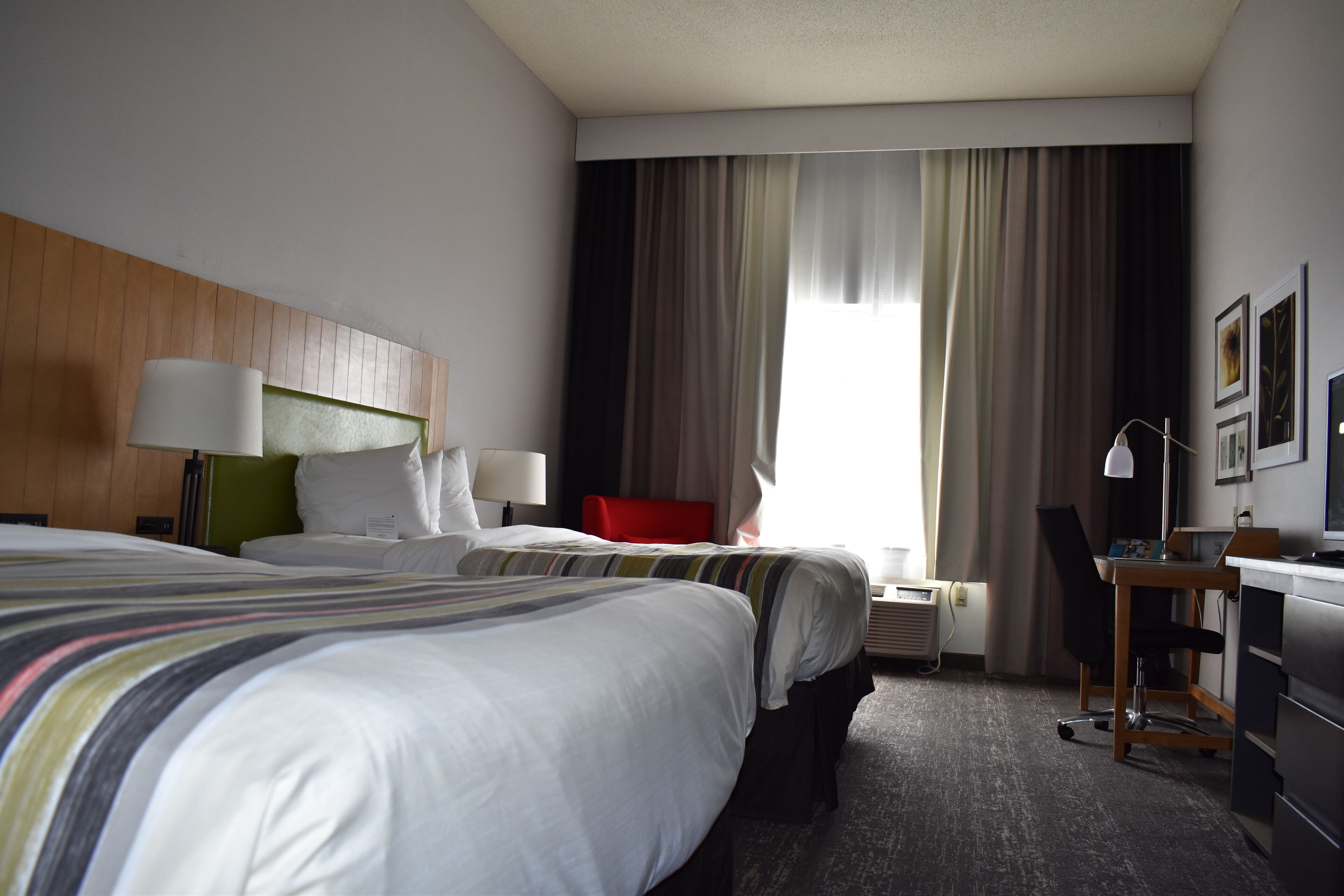 A hotel room with two beds, a desk, a chair, a lamp, and a window with curtains.