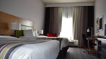 A hotel room with two beds, a desk, a chair, a lamp, and a window with curtains.