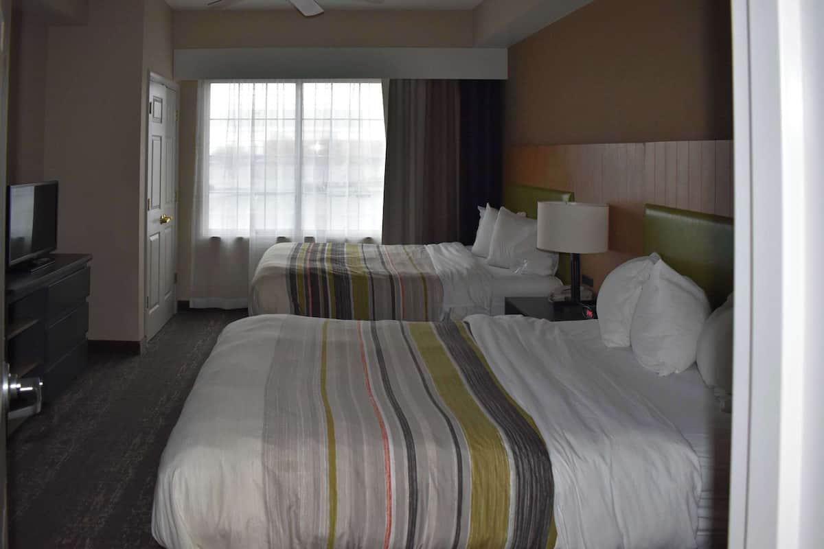 A hotel room with two beds, a TV, and a window with curtains.