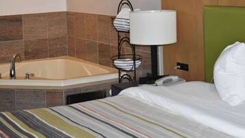 A hotel room with a bed, a bathroom with a sink, a lamp, and a telephone.