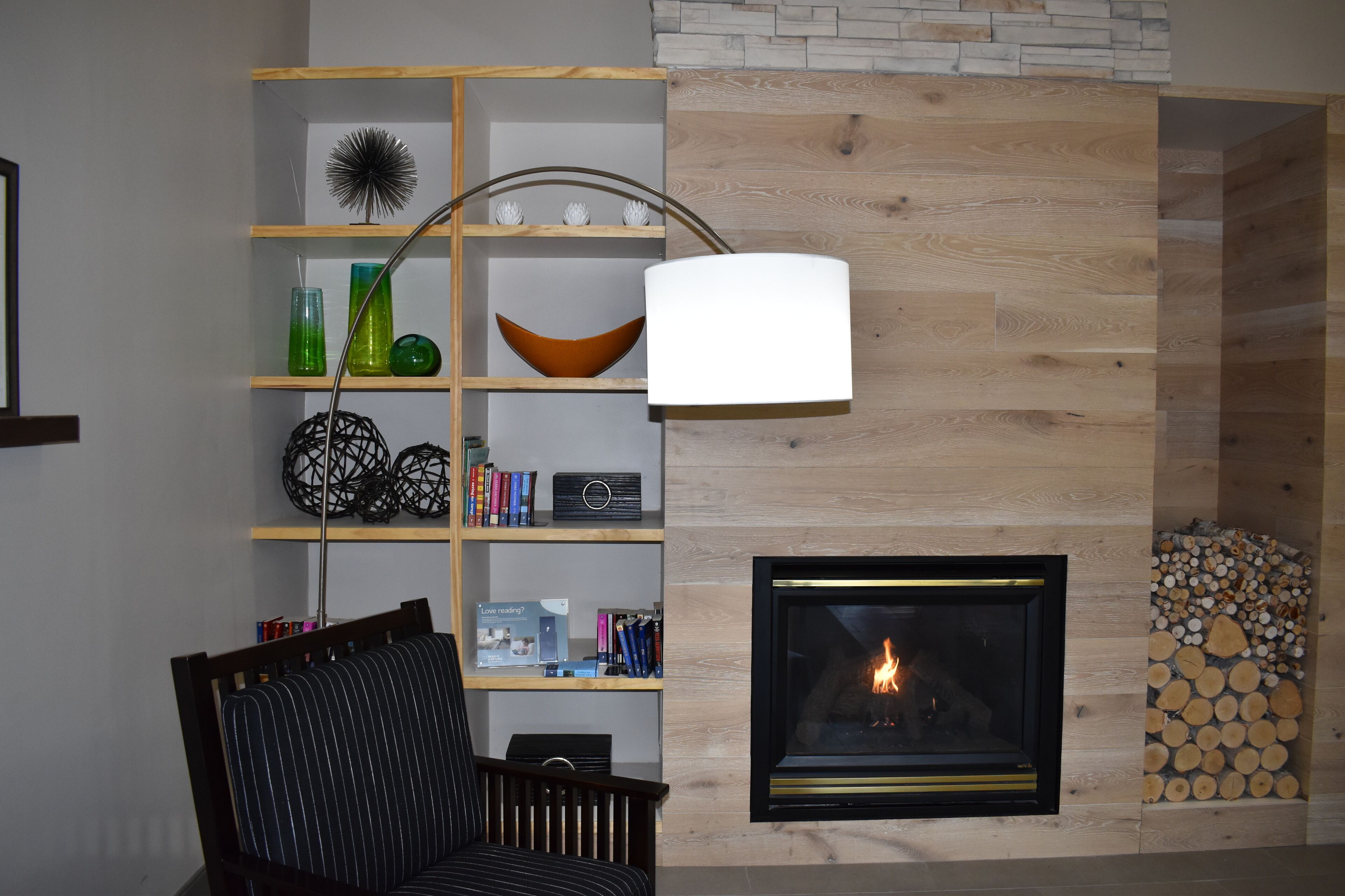 Una sala de estar acogedora con chimenea, estantes de madera con objetos decorativos, un sillón cómodo y una lámpara moderna.
