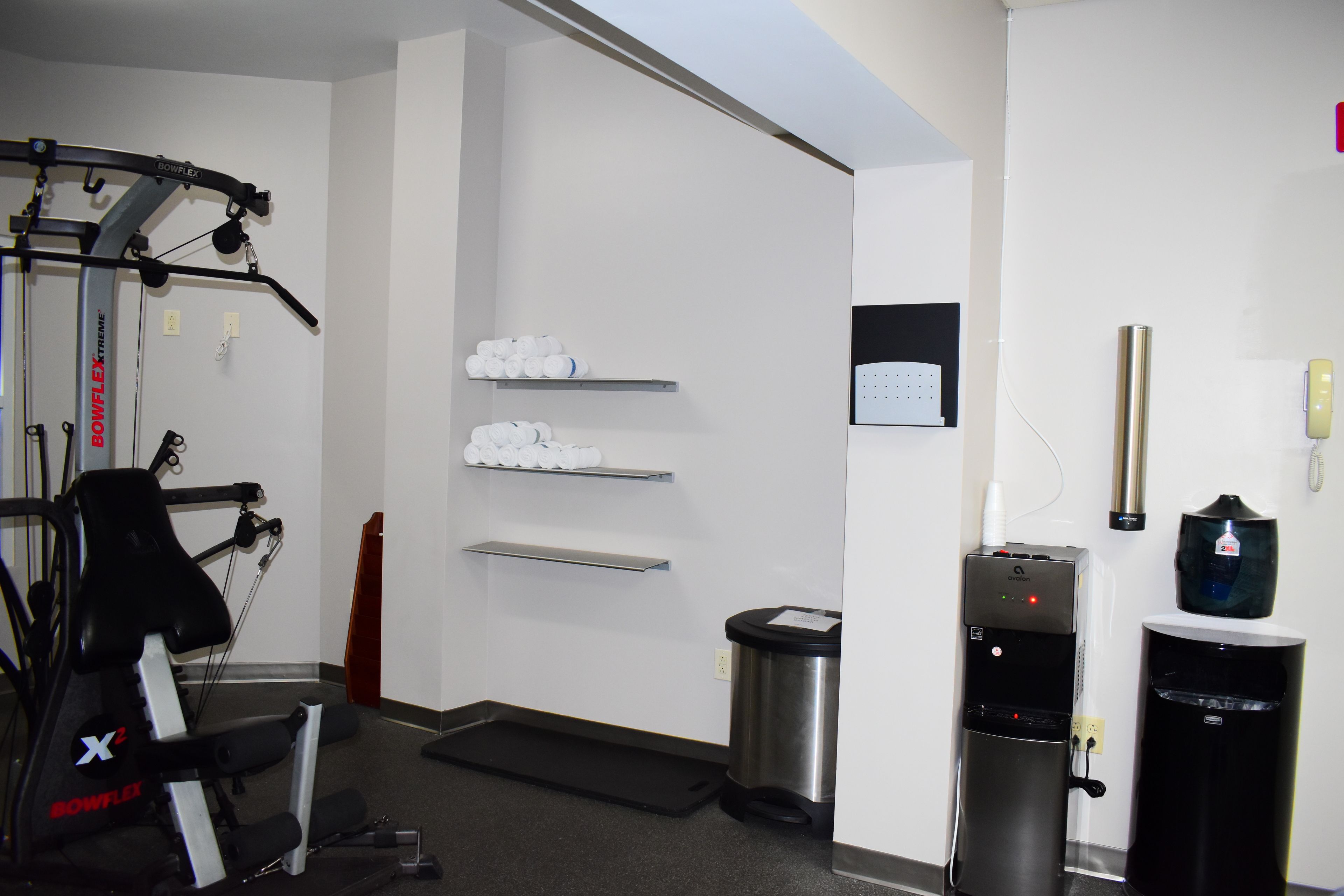 A gym with exercise equipment, a water dispenser, and a trash bin.