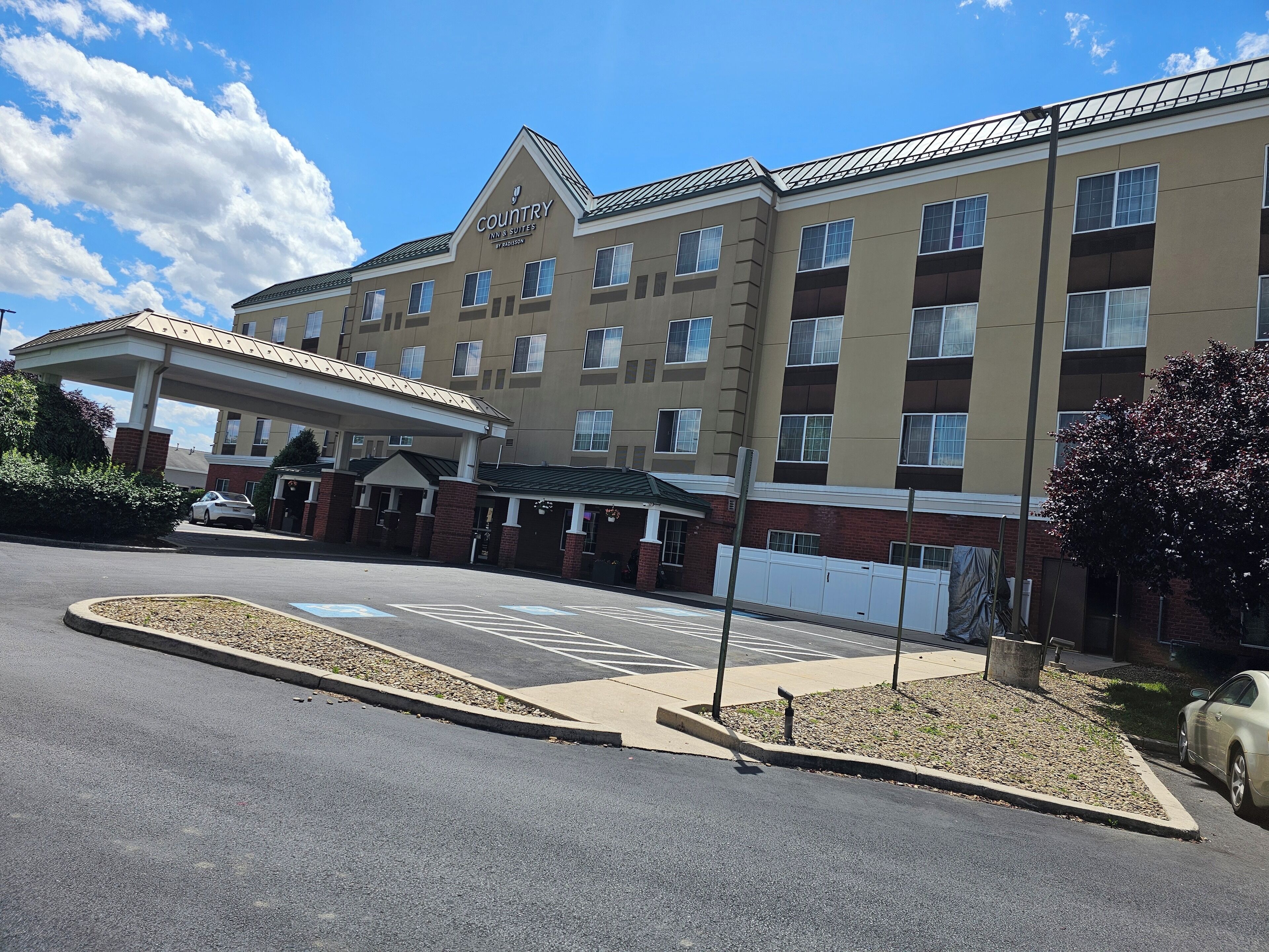 A Country Inn & Suites by Radisson building with a covered entrance, parking lot, and a landscaped area with a tree.