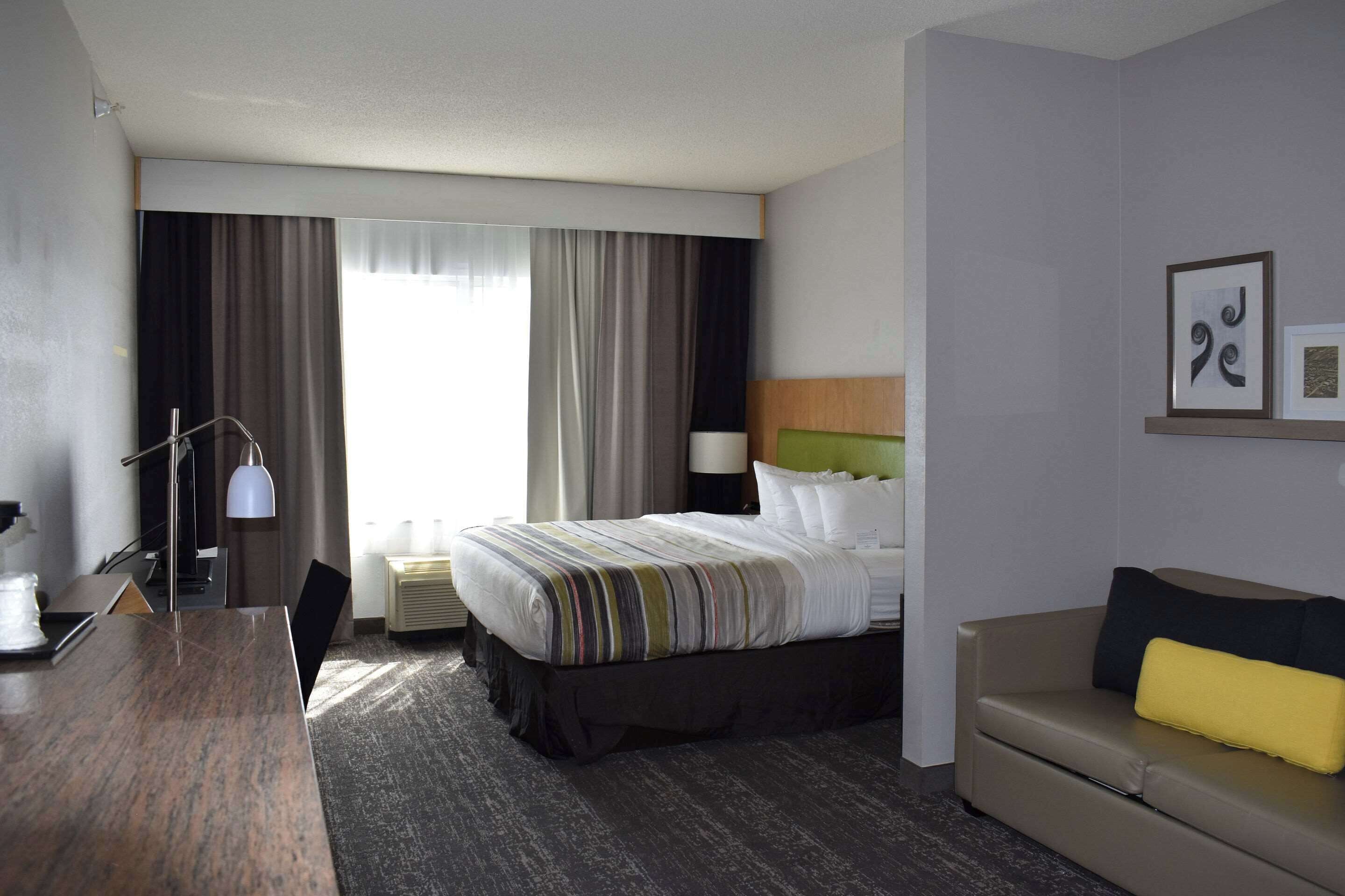 Une chambre d’hôtel avec un lit, un canapé, un bureau et une grande fenêtre avec des rideaux.