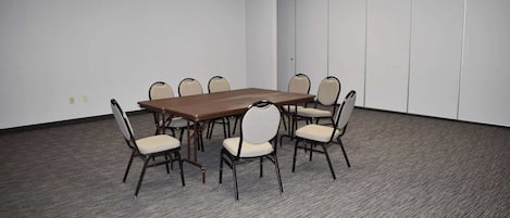 A conference room with a rectangular table surrounded by six chairs, carpeted floor, and white walls.