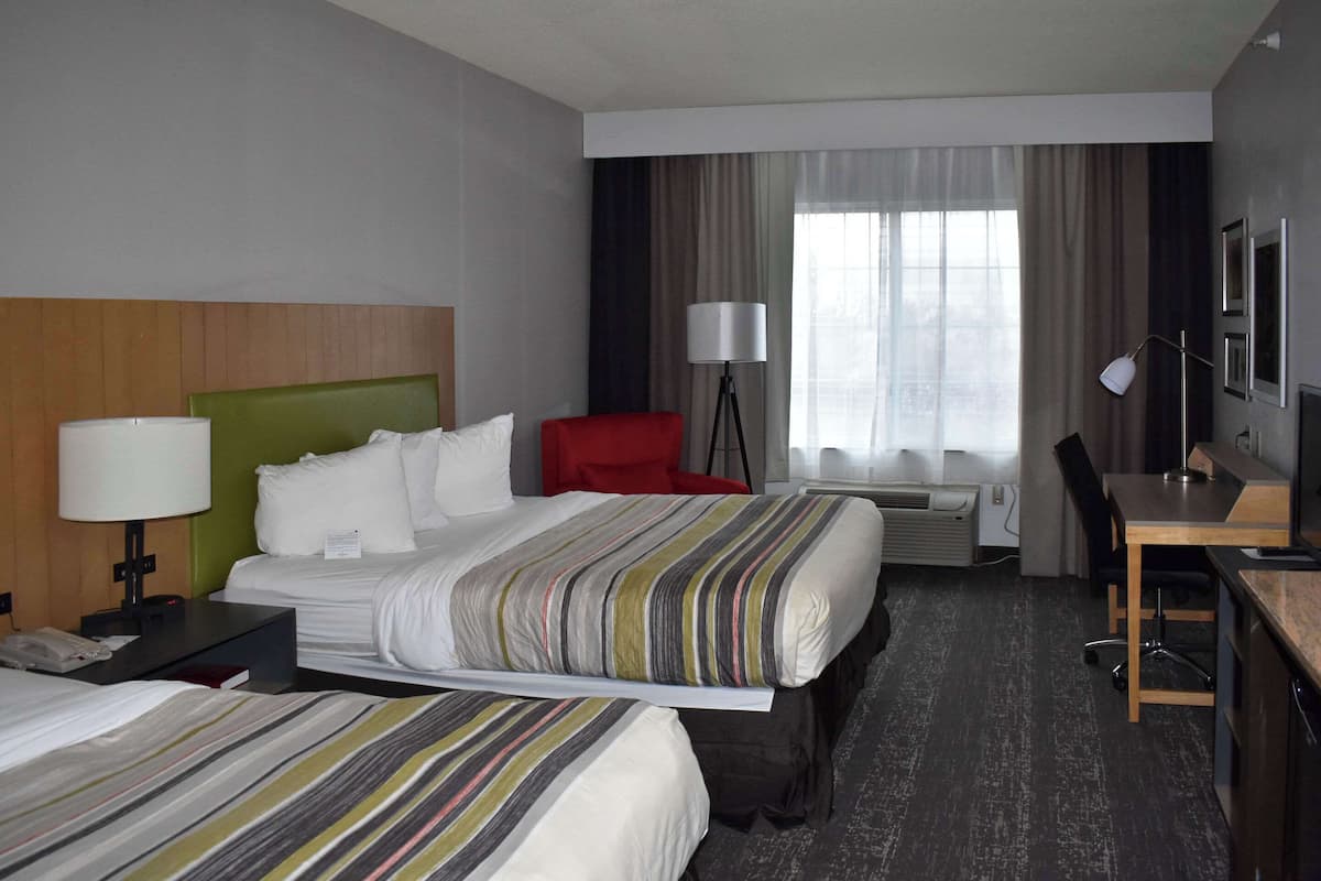 A hotel room with two beds, a desk, a chair, a lamp, and a TV.